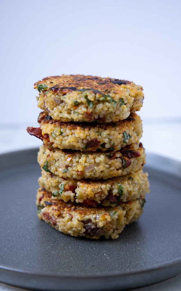 sundried tomato and basil quinoa patties stacked tall on a plate.