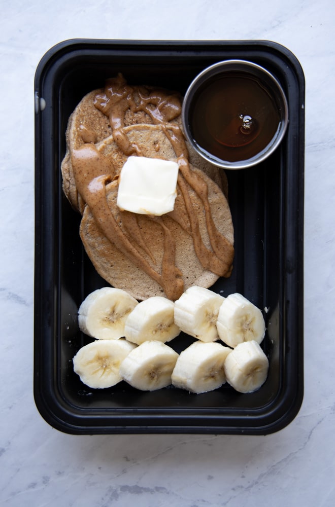 banana oat pancakes in a container with sliced bananas and maple syrup