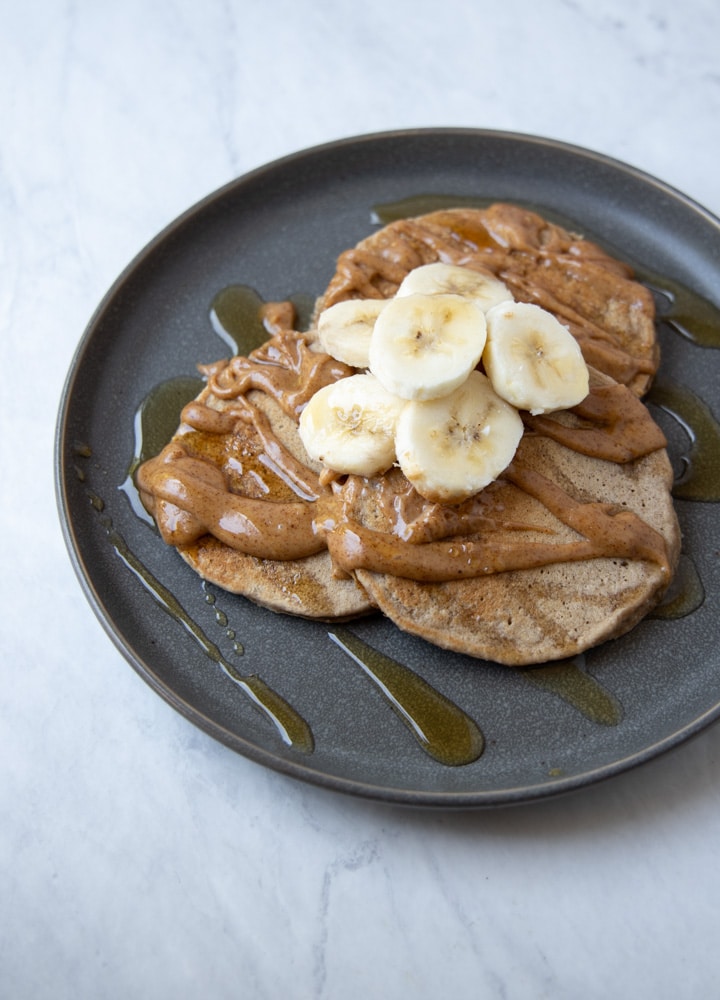 three banana pancakes on a plate, topped with peanut butter and sliced banana