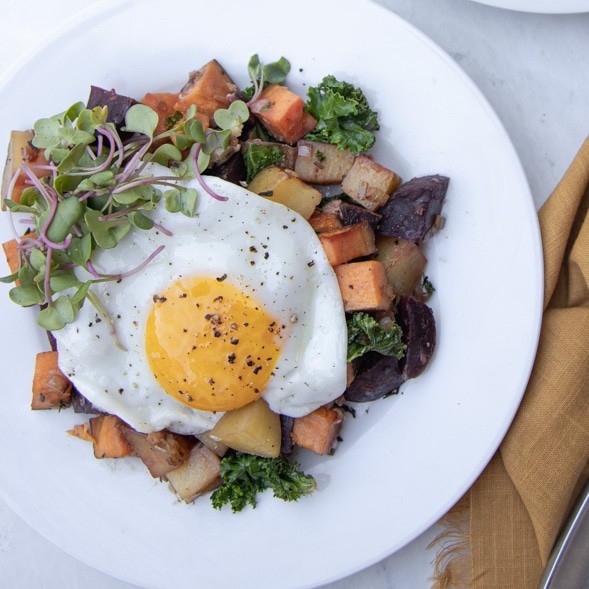 plate with root veggie hash and egg fried over easy on top.