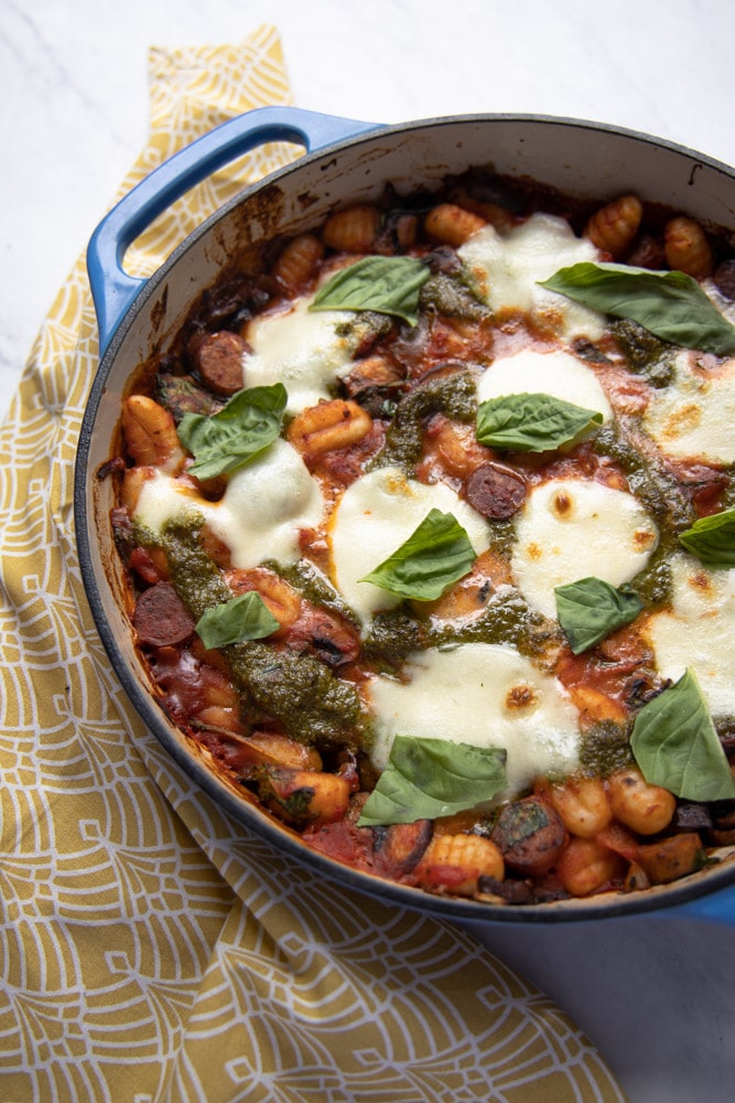 blue skillet with baked gnocchi and melted mozzarella on top garnished with basil leaves.