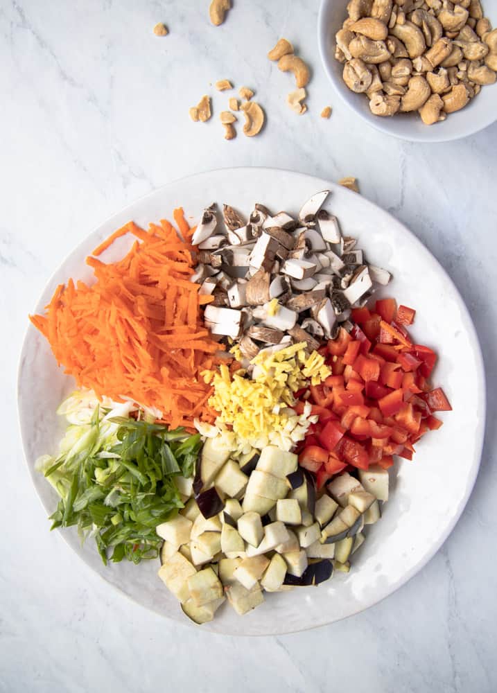 eggplant, mushrooms, peppers, carrot and green onions prepped and displayed on a big plate