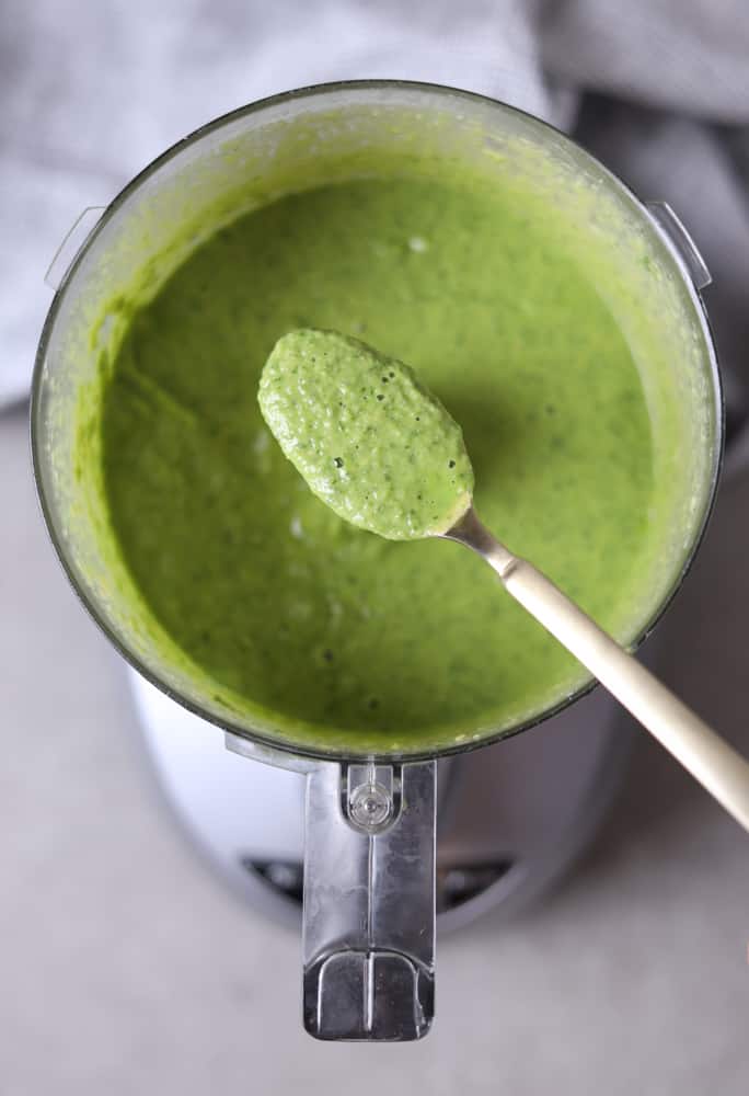 blended ingredients for sauce in food processor with sauce on a spoon