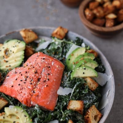 bowl of kale Caesar salad with salmon filet on top.
