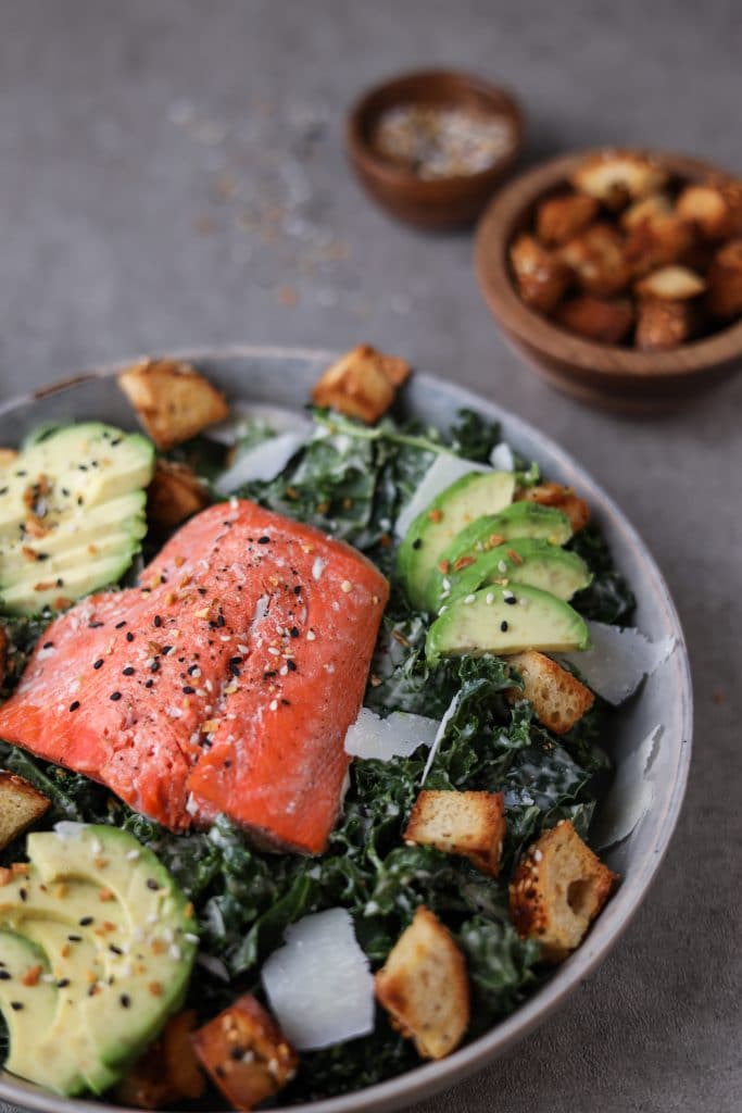 Close up of bowl of kale caesar with salmon.