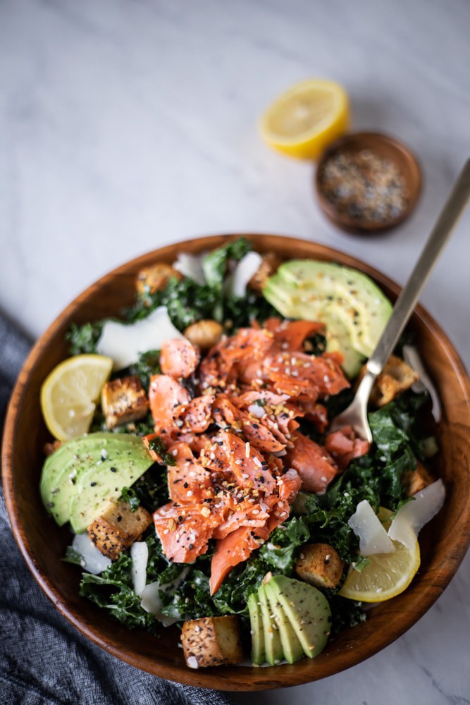 Close up of bowl of kale Caesar salad with flaked salmon over the top