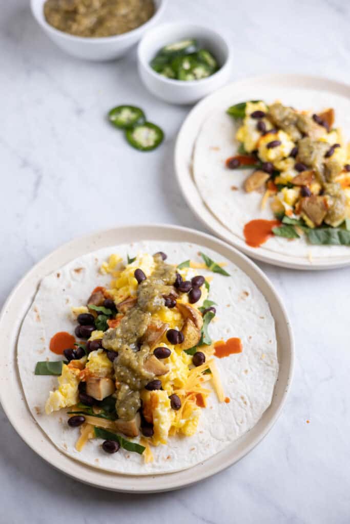 two plates with tortillas, scrambled eggs, potatoes and black beans