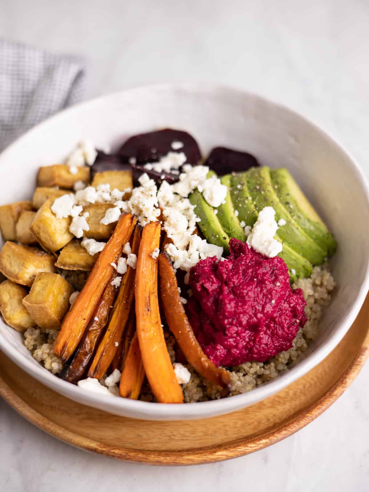 closeup bowl of quinoa, roasted carrots, beets, tofu, sliced avocado and beet hummus topped with feta cheese