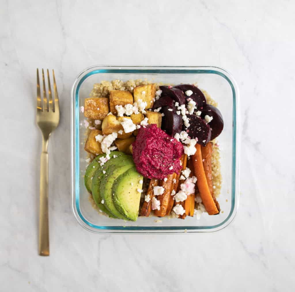 meal prep container of quinoa, carrots, tofu, beets and beet hummus topped with feta