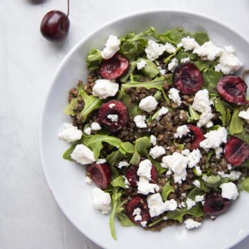 closeup image of bowl filled with cherry lentil salad topped with goat cheese