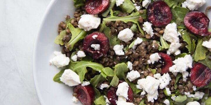 closeup image of bowl filled with cherry lentil salad topped with goat cheese