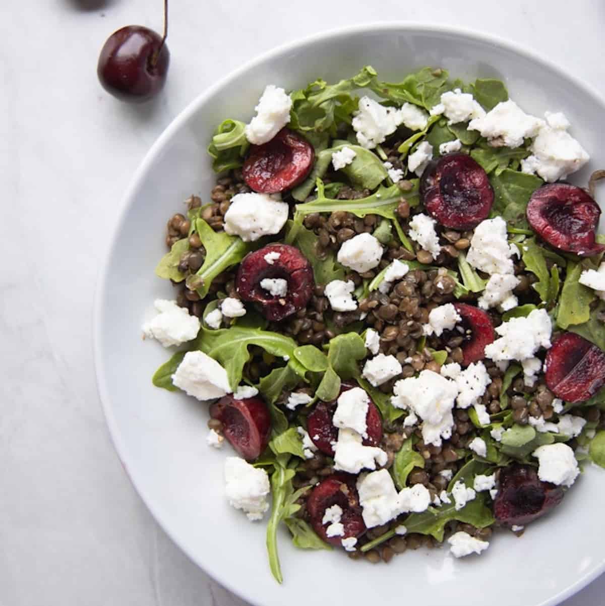 closeup image of bowl filled with cherry lentil salad topped with goat cheese