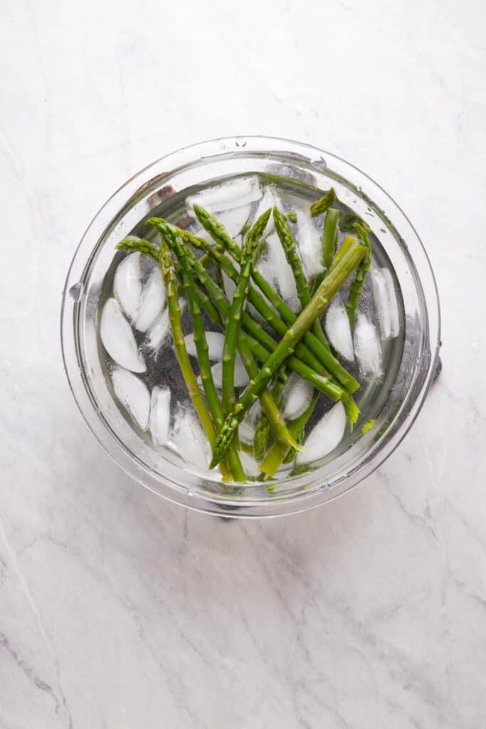 blanched asparagus spears in a bowl of ice water