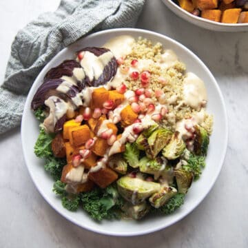 bowl full of quinoa, roasted squash, and Brussel sprouts topped with pomegranate seeds and maple tahini dressing