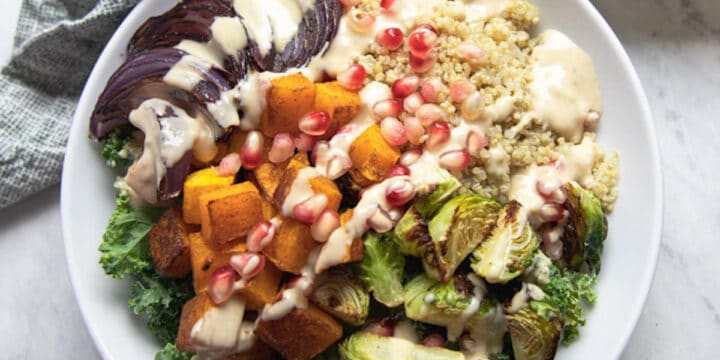 bowl full of quinoa, roasted squash, and Brussel sprouts topped with pomegranate seeds and maple tahini dressing