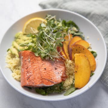 close up image of bowl of quinoa topped with salmon filet, sliced peaches and micro greens