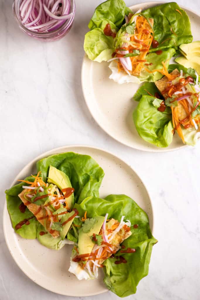 lettuce leaves on a plate filled with crispy tofu, pickled veggies, avocado and drizzled with sriracha