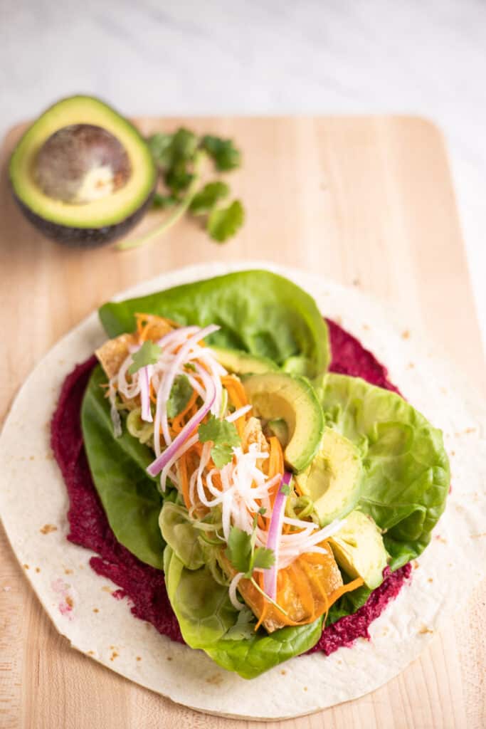 closeup of flour tortilla with beet hummus, tofu, pickled veggies and avocado