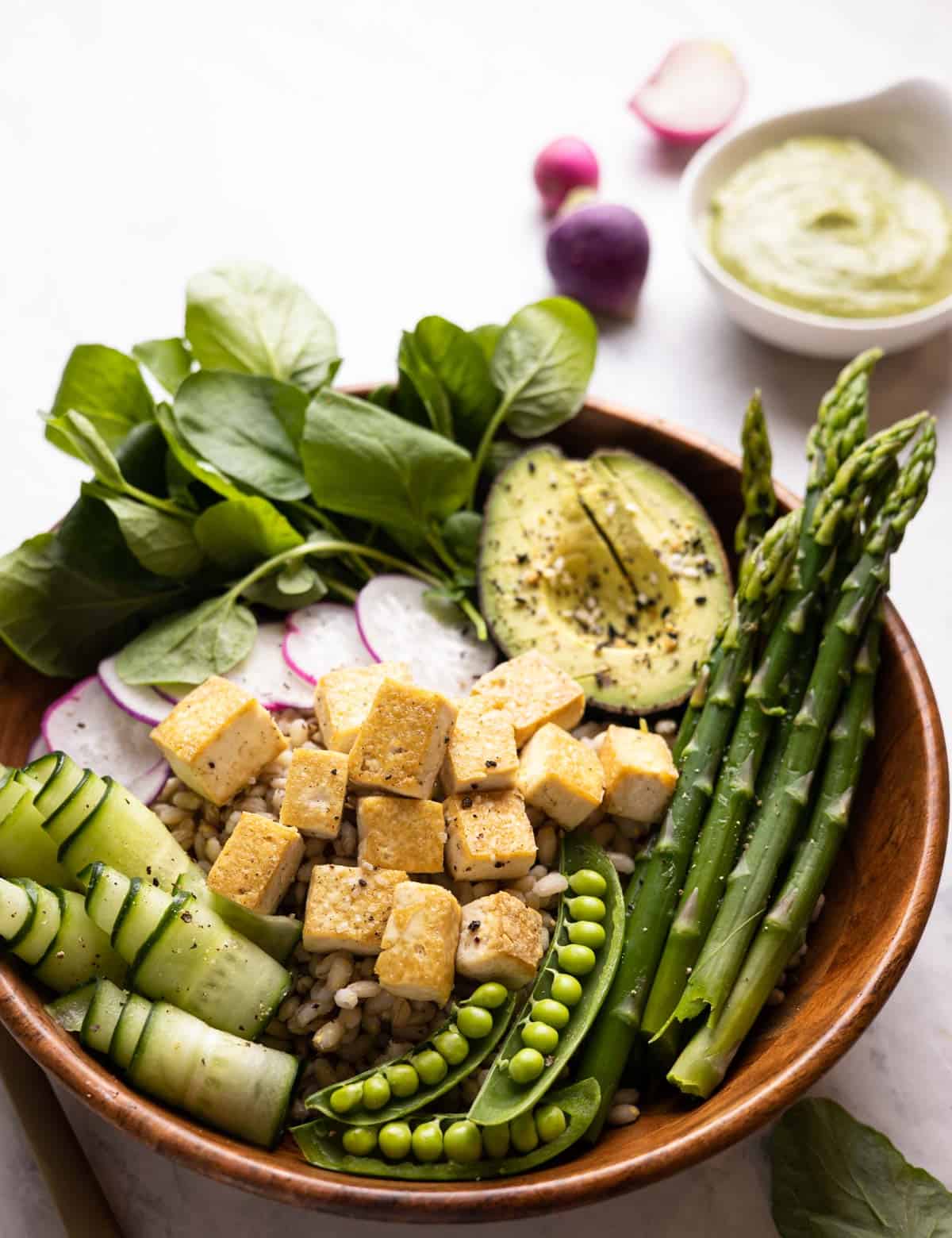 closeup of grain bowl in wooden bowl with ingredients layered on top of barley