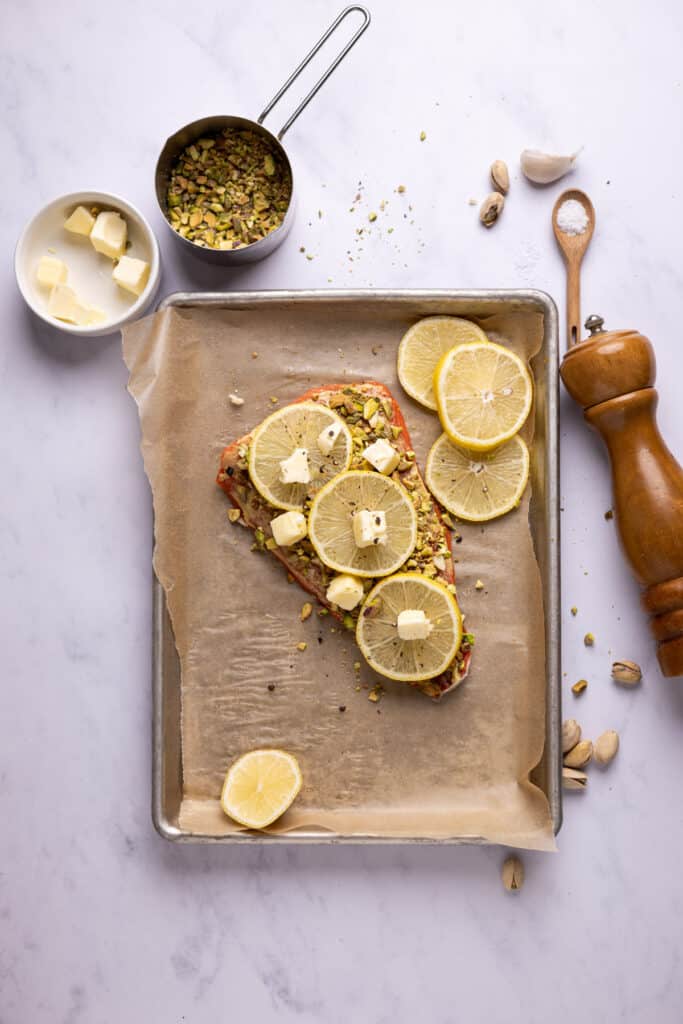 salmon topped with pistachios and lemon slices on a sheet pan