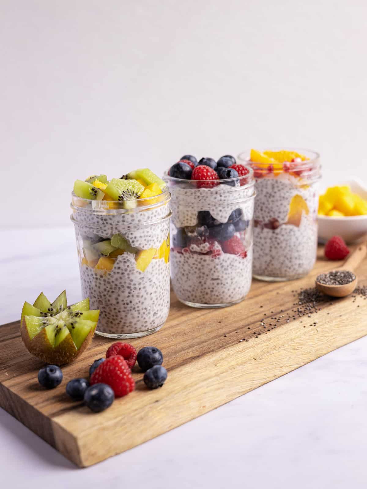 3 chia puddings layered in mason jars with fresh fruit