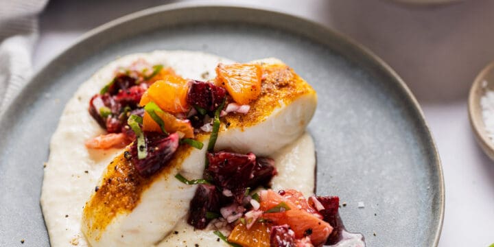 halibut filet on a bed of pureed cauliflower and topped with citrus salsa served on a blue plate.