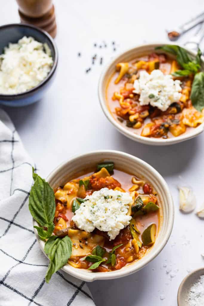 Two bowls of vegetarian lasagna soup with ricotta cheese mix on top.