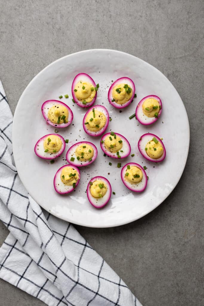 White platter full of beet deviled eggs topped with fresh chives.