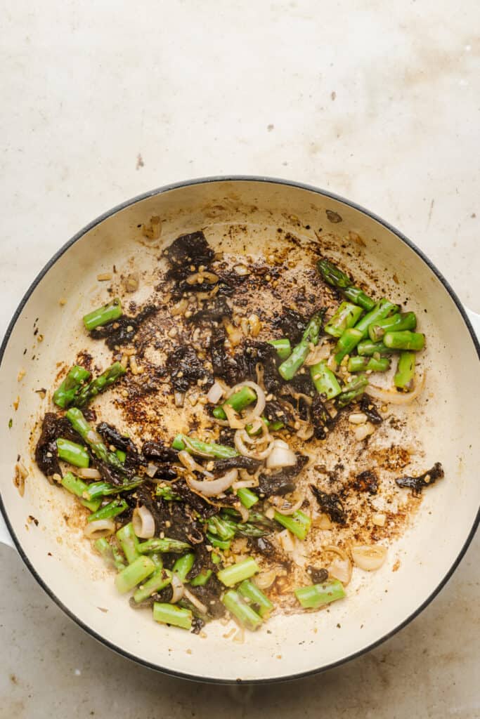 Asparagus and sundried tomatoes sauteed in a skillet.
