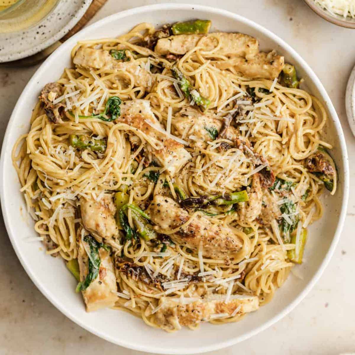 Sundried tomato pasta chicken in a white serving bowl topped with parmesan cheese.