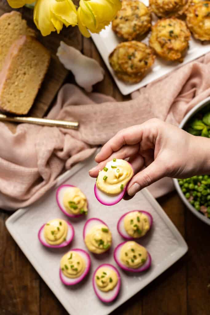 Hand grabbing a beet deviled egg from the platter.