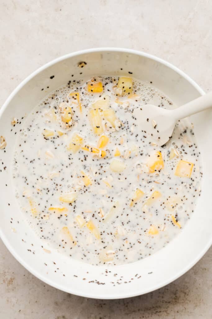 Ingredients to make tropical overnight oats stirred up in a bowl.