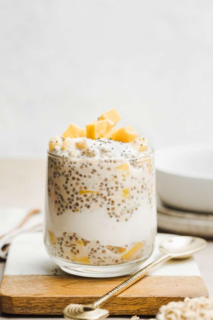 Glass filled with tropical overnight oats and topped with frozen fruit.